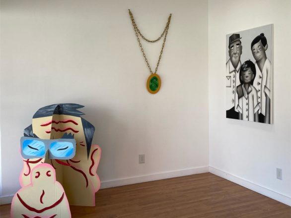 An art gallery containing a cardboard sculpture of a man's head, a hanging sculpture depicting a scaled-up necklace, and a painting of a family.