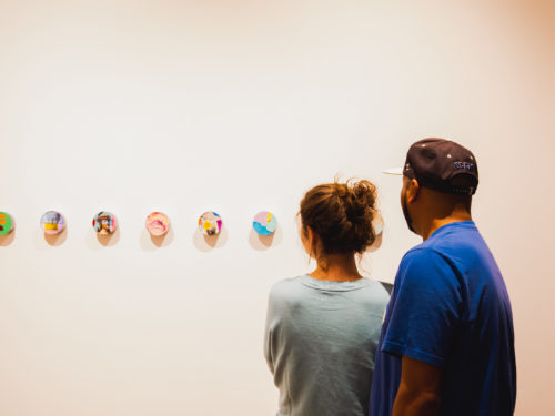 A couple examines a display of small paintings in an art gallery.