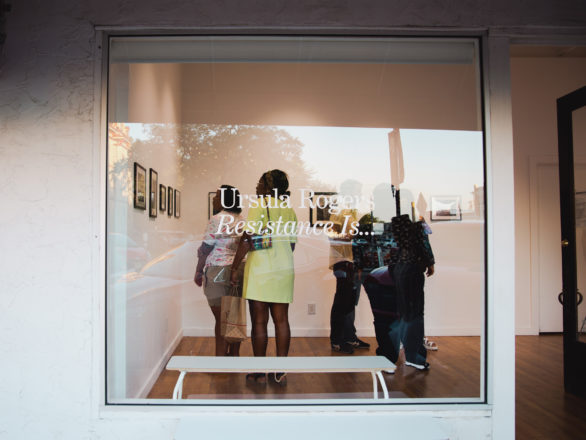 A woman examines photographs in a gallery. The text 