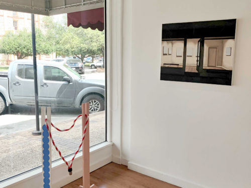 Artwork on display in a gallery: A sculpture made of wood and rope; and a painting of a storefront at night.